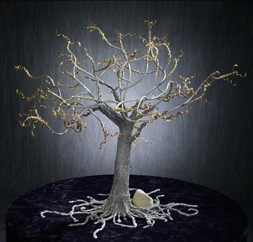 Sculpture of a tree in a gray and silver color, with gold material sculpted around all the branches like ribbons.