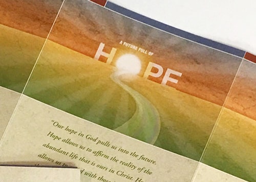 Close-up of a section of the outside of a print brochure featuring the word, 'Hope', with the letter 'O' depicted as the sun.