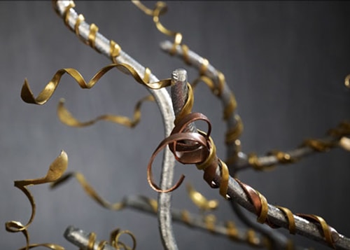 Close-up of the branches on a tree sculpture, with gold-colored pieces that look like ribbons entwined throughout.
