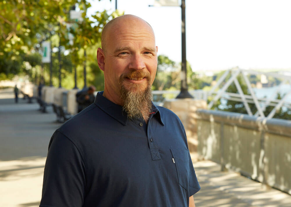 A middle-aged bald man with a beard and mustache wearing a navy blue polo shirt.