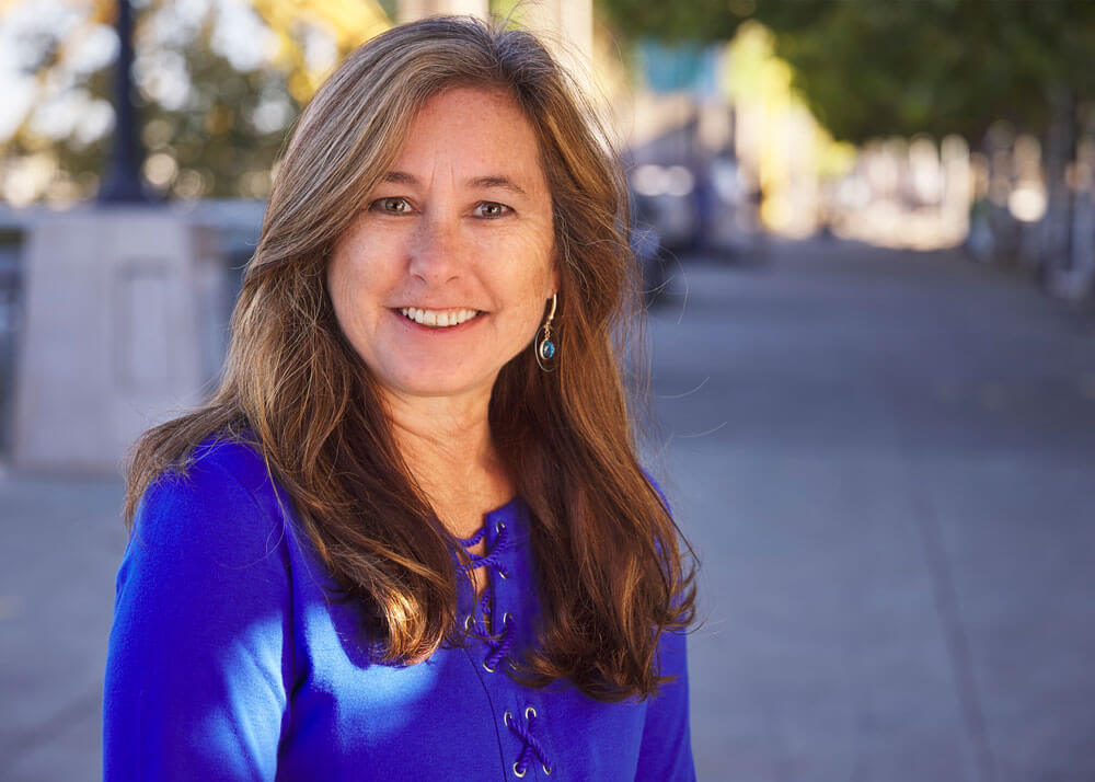 A middle-aged woman with long brown hair wearing a royal blue top.