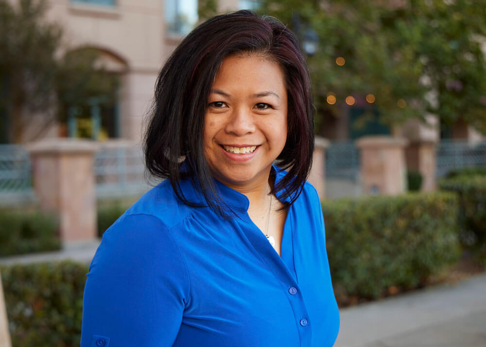 A woman with light brown skin, chin-length dark hair, and dark eyes wearing a blue top.